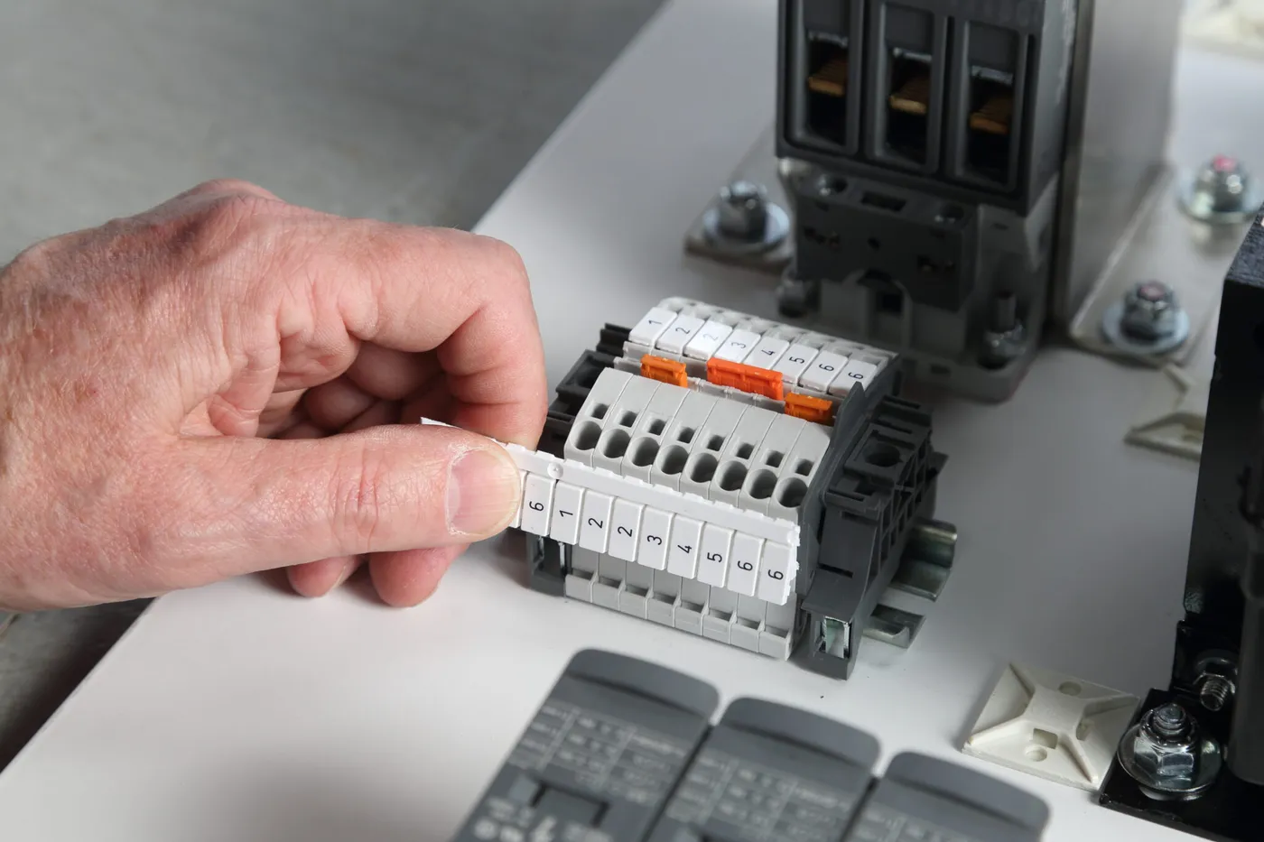 A hand snapping a printed marker card onto a row of terminal blocks