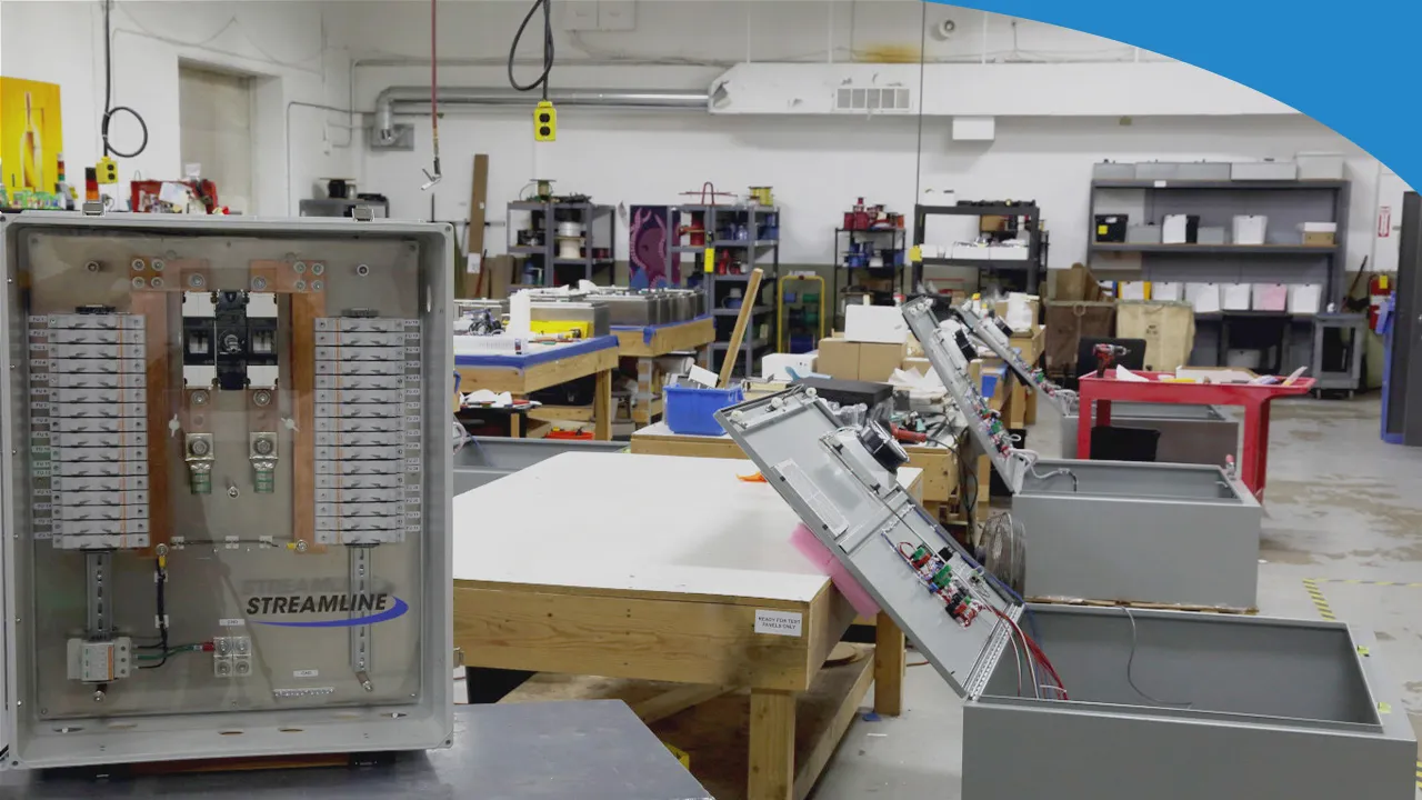 A Streamline solar combiner box with its door open, in a panel shop with enclosures and workbenches behind it